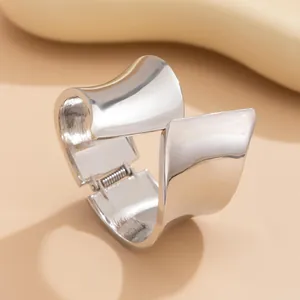 Close-up of asymmetric wide silver metallic bangle with irregular geometric design.