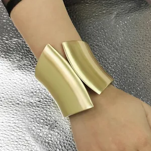 Detailed view of a wide asymmetrical matte gold cuff bracelet worn on a model's wrist