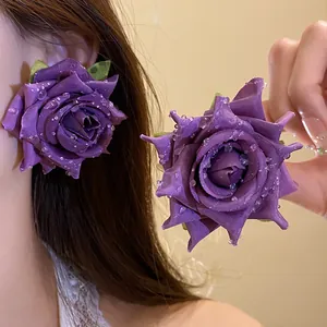 Macro vista di eleganti orecchini a rosa in tessuto viola con gocce di rugiada