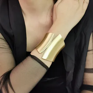 Detailed view of a wide asymmetric gold metal cuff bracelet worn on a female wrist