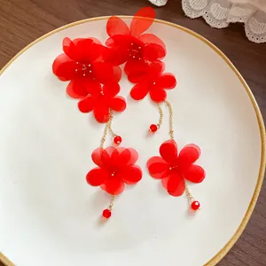 Close-up of elegant red chiffon flower tassel earrings with glass beads on a plate