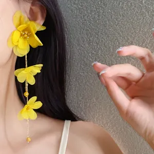 Detail view of yellow chiffon flower tassel earrings worn on a model's ear