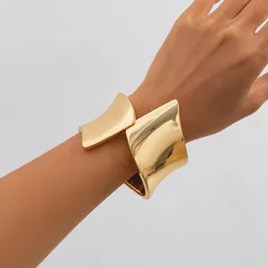 Close-up view of a wide asymmetric gold metal cuff bracelet worn on a woman's wrist.