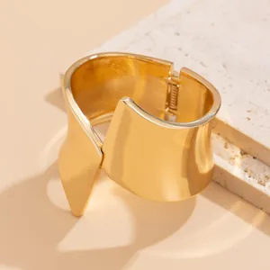 Close-up view of a high-shine gold asymmetric metal cuff bracelet with a hinged closure.