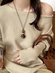 Detail shot of a vintage wood pendant necklace worn with a stylish beige knit sweater.
