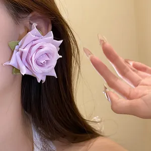 Primo piano di orecchini a lobo a forma di rosa in tessuto viola in stile vacanza.