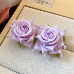 Dettaglio ravvicinato di orecchini a rosa in tessuto viola con perline a goccia.