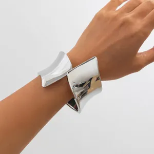 Detailed view of a wide asymmetric silver-toned metal cuff bracelet on a woman's wrist
