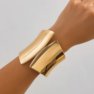 Detailed view of wide asymmetrical gold-tone metal cuff bracelet on wrist.