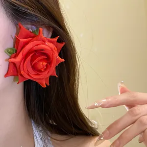 Primo piano di un orecchino a forma di rosa in tessuto rosso con gocce di rugiada.