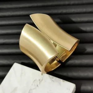 Close-up of a wide asymmetrical gold metal cuff bracelet featuring a brushed matte finish