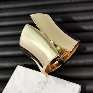 Close-up of a wide asymmetric gold metal bangle with high-polished mirror finish