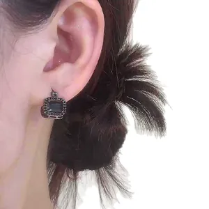Elegante dunkle Gothic-Ohrringe mit quadratischen Strasssteinen am Ohr eines Models