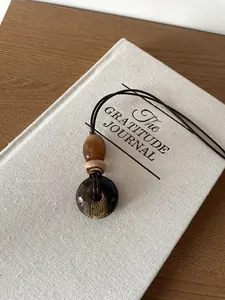 Detailed macro view of a vintage wood-pattern round pendant on a linen gratitude journal.