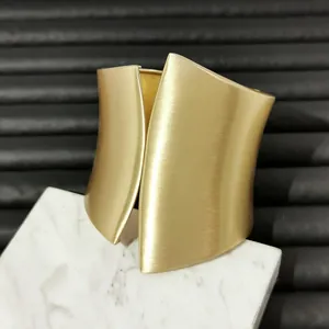 Close-up of a wide asymmetric gold metal cuff bracelet with a brushed matte finish