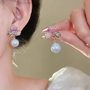 Detailed view of elegant gold-toned flower drop earrings with pearls and pink crystal accents