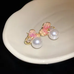 Macro detail of elegant gold-toned stud earrings featuring pink crystal and white pearl