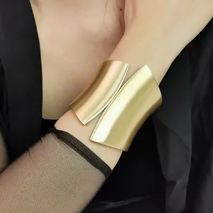 Close-up view of a wide asymmetrical gold metal cuff bracelet with matte brushed texture on wrist