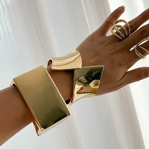 Detail of wide asymmetric gold-plated metal cuff bracelet and multi-layer rings