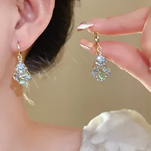 Close-up of elegant rhombus drop earrings with sparkling crystals and green stones