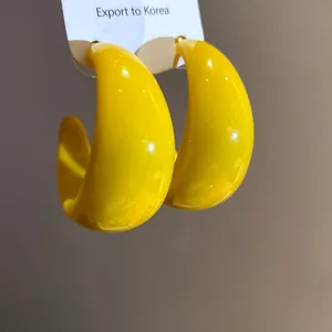Primo piano dettagliato di orecchini a cerchio in resina giallo vivace a forma di C lucidi