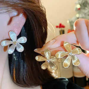 Primer plano de elegantes pendientes de flor con textura metálica cepillada y centro brillo