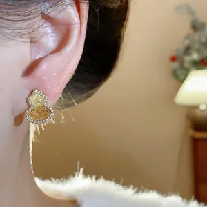 Detailed view of a gold-plated gourd stud earring with sparkling zircon inlays worn on ear