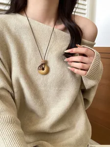 Detailed view of a retro circular pendant necklace worn with a beige knit sweater