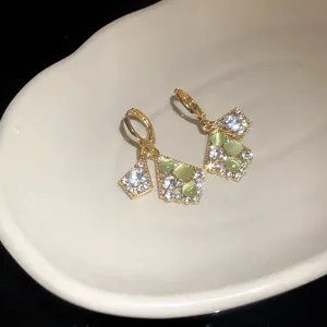 Close-up detail of gold earrings with green cat-eye stones and sparkling crystals