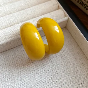 Dettaglio macro di orecchini a cerchio a C in resina gialla su tessuto beige