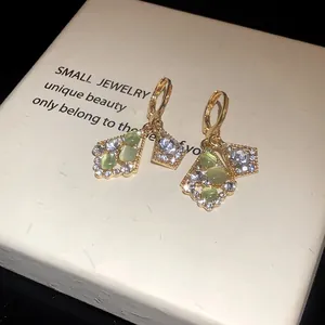 Close-up detail of gold-tone earrings with green cat's eye stones and crystals