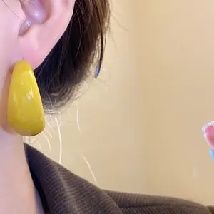 Dettaglio di un orecchino in resina giallo brillante a forma di C con finitura lucida