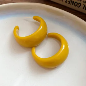 Primo piano di orecchini a cerchio a forma di C in resina giallo brillante con finitura lucida