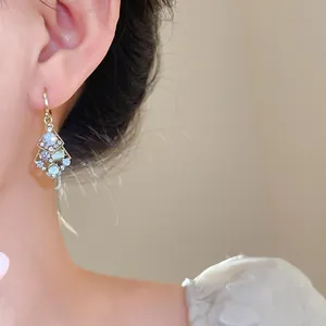 Close-up of elegant gold rhombus earrings with sparkling crystals and opals on ear.