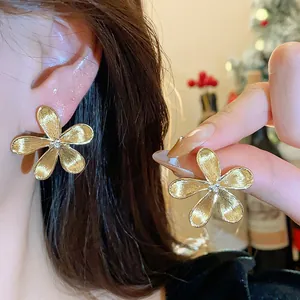 Detalle de elegantes pendientes de botón con forma de flor dorada de cinco pétalos texturizados