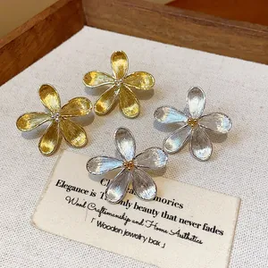 Primer plano de pendientes de botón de flor en oro y plata en un joyero de madera.
