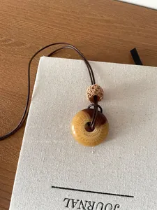 Macro detail of a retro wooden ring pendant necklace resting on a white fabric journal