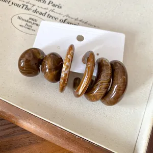 Macro view of vintage brown marbled acrylic C-shape stud earrings on a white jewelry card