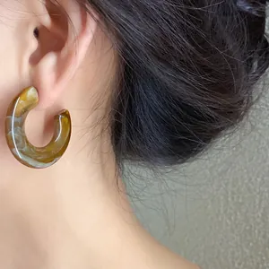 Close-up detail of a brown marbled acrylic C-shaped hoop earring on an Asian model