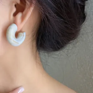 Close-up of marble-patterned acrylic C-shaped stud earring worn on ear
