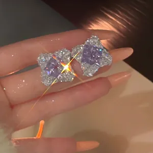 Close-up of sparkly purple diamond-shaped zircon earrings with silver needle posts.