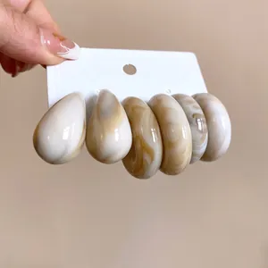 Close-up of acrylic marble earrings set in warm brown and beige mottled patterns