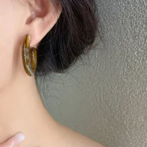 Macro view showing the marbled texture of brown acrylic C-shaped earrings worn by a model