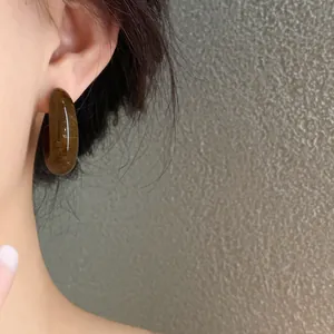 Detailed close-up showing retro amber marbled acrylic C-shape hoop earrings worn on ear.