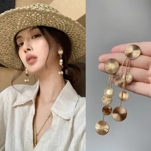 Close-up detail of elegant golden sunburst textured round disc tassel drop earrings for women