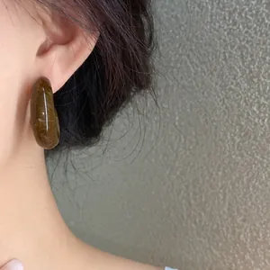 Close-up detail of a marbled acrylic C-shaped stud earring worn on an Asian model's ear.