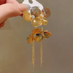 Exquisite macro detail of gold-plated flower earrings featuring long metal chain tassels