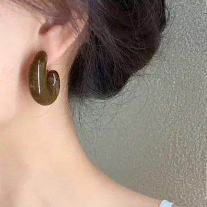 Detailed close-up shot of a marbled brown acrylic C-shaped earring worn by a model