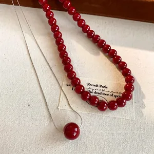 Minimalist set of red pearl bead necklace and silver chain pendant on beige canvas