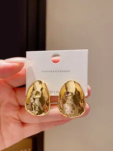 Close-up detail of irregular gold metallic stud earrings with high-gloss finish